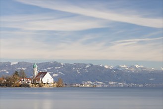 Picturesque church of St. George on the lakeshore in front of snow-covered Pfänder on a clear