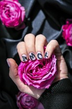 AMOR word on nails manicure hold Pink rose flower on black silk fabric. Love, Minimal flat lay