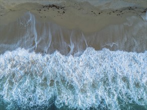 A top down view of the golden sand Rotonda Beach in Tropea with turquoise water and waves crashing