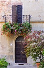 Half closed shutters during siesta on a balcony decorated by blooming flowers in Pienza, Tuscany,