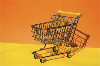 Empty shopping trolley cart on colorful orange yellow background. Copy space for your text. Online