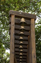 Art display of a wooden rack with many brass bells and trees behind