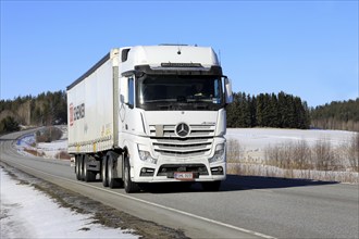 White Mercedes-Benz Actros 2653 truck pulls DB Schenker semi trailer along highway on a sunny day