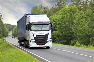 White Iveco S-Way truck pulls curtainside semi trailer uphill along highway 52 on a day of summer.