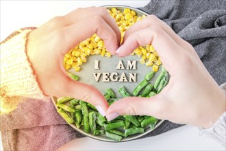 Female hands in shape of heart love I AM VEGAN text in plate. Veganism, vegetarian healthy