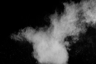 Freeze motion of white dust particles on black background. White powder explosion