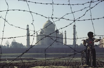 08.02.2004, Agra, Uttar Pradesh, India, Asia, A boy stands with his bicycle behind a barbed wire