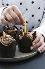 Female hands making Delicious chocolate cupcakes with cream on dark background. Three chocolate