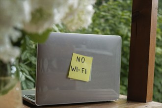 Paper note with text NO WI FI in laptop garden background. Concept of digital detox, unplugging