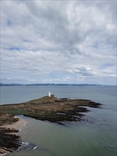 A view of the Mumbles Lighthouse in Swansea Bay at low tide with algae and rocks in the foreground