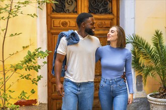 Multi-ethnic couple leaving the house together with a smile, embraced from behind