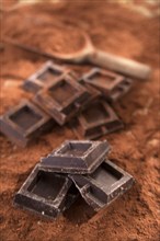 Presentation of some cubes of dark chocolate on a bed of cocoa