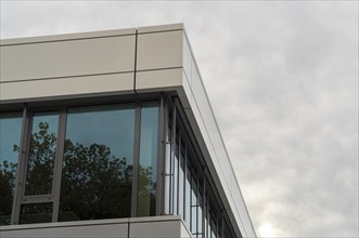 Modern office building with glass windows reflecting trees on a cloudy day