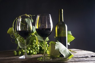 Glass of red wine with bottle and bunch of sour grapes on a black background