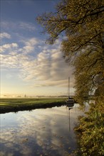 Autumn trees along a canal with a sailing boat seen from the castle estate in the Dutch village