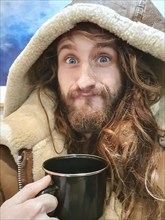 Portrait shot of a funny young man with a camping tin tea cup in his hand, looking at camera and