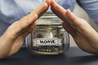 Unrecognizable woman holding Saving Money In Glass Jar filled with Dollars banknotes. HOME