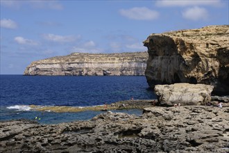 Tourists enjoy the refreshing water under yellowish-brown limestone cliffs, San Lawrenz, Malta,