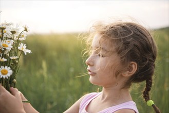 Portrait cute child girl with a bouquet of chamomile in summer on a green natural background. Happy