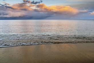 Background of gentle waves on golden sand beach with ocean and colorful sunset sky behind