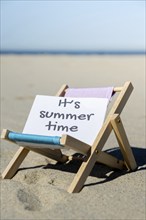 IT'S SUMMERTIME text on paper greeting card on background of beach chair lounge summer vacation