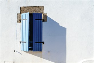 Old window with wooden blue painted shutters on white painted wall