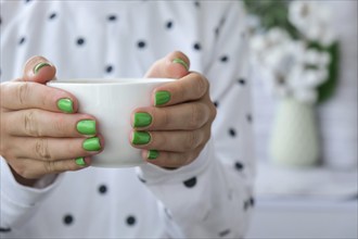 Manicured female hands with stylish green nails holding cup of coffee. Take a break for coffee