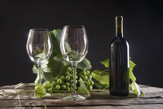 Glass of red wine with bottle and bunch of sour grapes on a black background