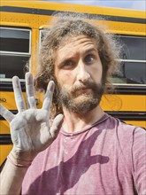 Close up portrait shot of a funny looking young man with long hair, showing a dirty dusted hand