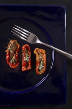 Presentation portion of dried tomatoes with rosemary on plate black