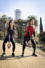 Man and woman exercising with dumbbells during a workout in the park