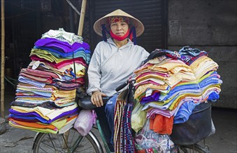 Vietnamese woman with nón lá conical hat selling textile and clothes from bicycle in the city Ninh