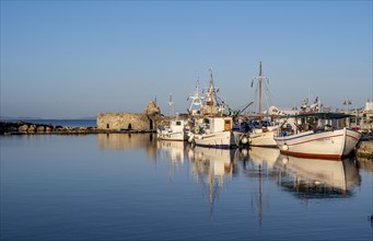 Fishing boats in the harbour and ruins of the Venetian castle, reflected in the sea, at sunset,