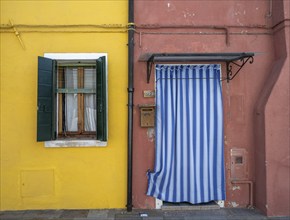 Red and yellow house facade with entrance door with blue and white curtain and windows, colourful