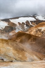 Hot springs and steaming stream between colourful rhyolite mountains with snowfields, Hveradalir