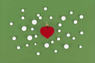 Red heart shaped Christmas tree bauble surrounded by snowballs on green background