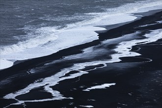 Foamy white waves and icy surfaces on the black pebble beach Skogarsandur, near Dyrholaey,