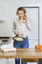 Happy young woman holds skillet with fried eggs and toasts in hand