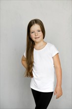 Cute young child with long hair in white t-shirt and black sweatpants posing