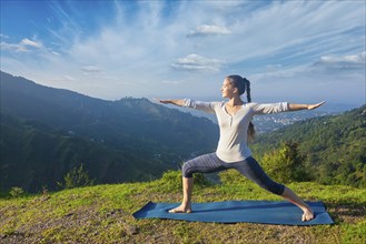 Yoga outdoors, sporty fit woman doing yoga asana Virabhadrasana 2, Warrior pose posture outdoors in