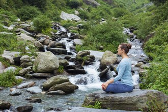 Woman in Hatha yoga asana Padmasana outdoors at tropical waterfall