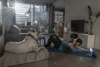 Fit man training at home with his dog. Environment illuminated with rays of sunlight