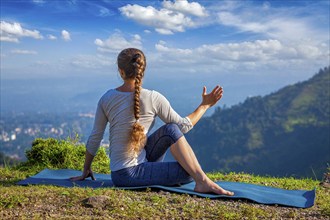 Hatha yoga outdoors, woman doing yoga asana Parivrtta Marichyasana or ardha matsyendrasana, seated