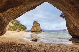 View from a cave opening onto a sandy beach and a solitary rocky outcrop in the sea, Cathedral