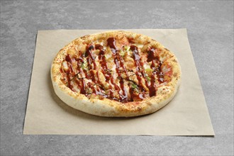 Barbecue pizza with bacon and spring onion on parchment paper