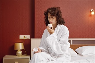 Woman in bathrobe opened jar of cream and inhales its fresh aroma