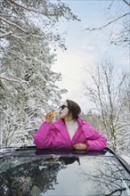 Funny woman drinking champagne leaning out of the car hatch in winter woods