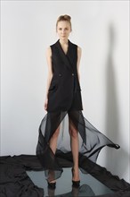 Fashion model in designers black sleeveless jacket and flying transparent skirt posing near the