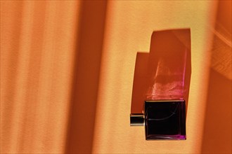 Bottle of perfume for men on orange background under sun light from the window