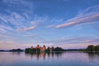 Trakai Island Castle in lake Galve, Lithuania on sunset with dramatic sky reflecting in water.